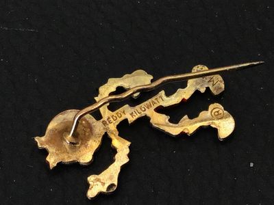 Sale Photo Thumbnail #133: Small lot of vintage items including an advertising lapel pin featuring Reddy Kilowatt, marked on the back with REDDY KILOWATT and a registered trademark symbol, measuring under 1 inch tall. Also includes a silver-tone filigree necklace featuring clear rh