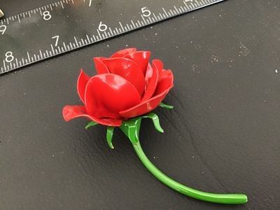 Sale Photo Thumbnail #137: Vintage bright red enamel rose brooch with a long green stem and leaf detailing underneath. Features a standard pin back with rollover safety clasp. Measures approximately 3 inches in length. In good vintage condition with minor wear to the finish consist