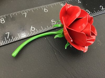 Sale Photo Thumbnail #138: Vintage bright red enamel rose brooch with a long green stem and leaf detailing underneath. Features a standard pin back with rollover safety clasp. Measures approximately 3 inches in length. In good vintage condition with minor wear to the finish consist