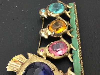 Sale Photo Thumbnail #145: A vintage gold-tone costume jewelry brooch depicting a mother hen with three chicks walking along a green painted bar. Features colorful faceted oval glass rhinestones in purple, pink, yellow, and blue, with tiny rhinestone eye details. Pin back clasp on 