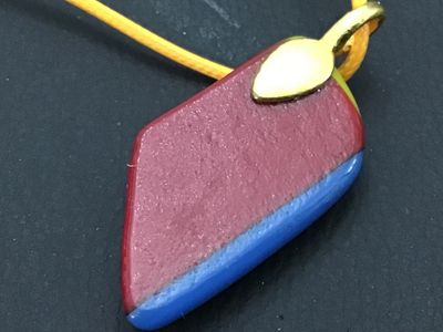 Sale Photo Thumbnail #43: Artisan handcrafted fused glass pendant featuring layered geometric colors including orange, yellow, blue, black, and matte burgundy. Attached with a gold-tone bail to a yellow cord necklace. In good condition with no visible chips or cracks. Measures app