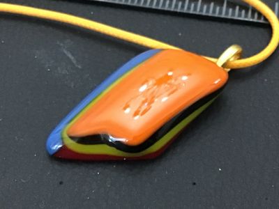 Sale Photo Thumbnail #41: Artisan handcrafted fused glass pendant featuring layered geometric colors including orange, yellow, blue, black, and matte burgundy. Attached with a gold-tone bail to a yellow cord necklace. In good condition with no visible chips or cracks. Measures app