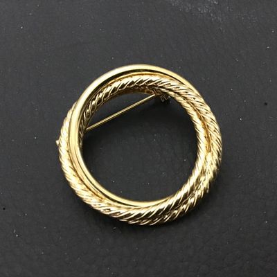 Sale Photo Thumbnail #56: Gold-tone circular brooch featuring a classic twisted rope motif interwoven with a smooth polished ring. Features a standard pin back with a safety clasp. Appears to be in very good vintage condition with minor surface wear typical of age.
