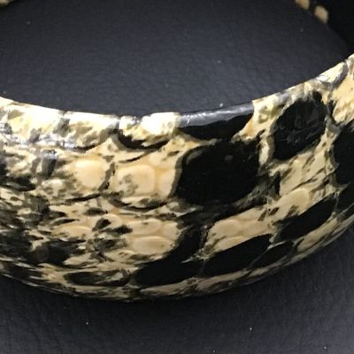 Sale Photo Thumbnail #61: A wide, chunky bangle bracelet featuring a black and cream python/snakeskin pattern finish over a hard core. The interior is lined in black and retains a remnant of an old price tag. Shows light vintage wear consistent with age.