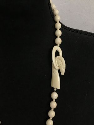 Sale Photo Thumbnail #96: A vintage cream-colored beaded necklace featuring a hand-carved focal element shaped like a ram or goat head hooked onto an oval loop. Made of carved bone, faux ivory, or composite resin beads strung together. Good condition with light vintage wear.