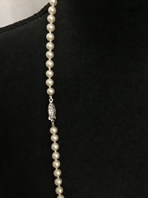 Sale Photo Thumbnail #100: A classic single strand faux or cultured pearl style necklace featuring hand-knotted construction between round cream-colored beads. Finished with a decorative silver-tone filigree marquise fishhook clasp. Overall good condition with minor vintage wear vi