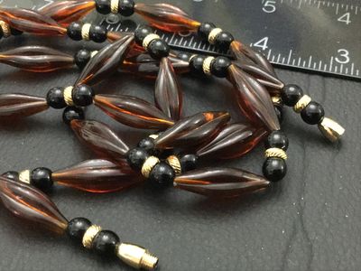 Sale Photo Thumbnail #115: Long vintage beaded strand necklace featuring amber-toned fluted/marquise acrylic beads alternating with black round beads and textured gold-tone spacers. Features a threaded barrel clasp closure. Measures approximately 30+ inches in length. In good vinta