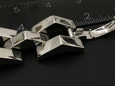 Sale Photo Thumbnail #124: Bold modern silver-tone wide link bracelet featuring stylized chevron/peak top panels with textured open undersides and a fold-over clasp. Features a small heart symbol stamped near the clasp. Bracelet measures approximately 7.5 to 8 inches in length and 