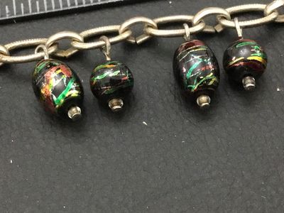 Sale Photo Thumbnail #175: A silver-tone chain bracelet featuring dangling black glass beads decorated with colorful metallic foil flecks/swirls in green, red, and gold tones. Features a textured toggle clasp closure. Measures approximately 7.5 to 8 inches in overall length. Good v