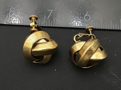 Sale Photo Thumbnail #181: Pair of vintage gold-tone clip-on earrings featuring a textured love knot design with combination screw-back and clip closures. Marked with patent number 2784478 (or similar) on the back. Each earring measures approximately 3/4 inch in diameter. Good vint