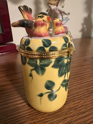 Sale Photo Thumbnail #254: Hand-painted porcelain trinket box featuring a yellow base with green ivy leaves and a lid decorated with a nest of birds, complete with a hinged brass rim.