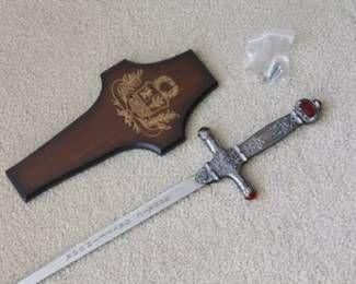 Decorative replica sword with an ornate hilt featuring red faux-gem accents, accompanied by a wooden wall-mounting plaque with a...