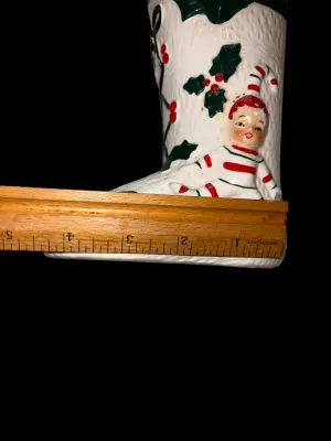 Sale Photo Thumbnail #137: Charming vintage UCAGCO (United China & Glass Company) ceramic Christmas boot planter featuring a whimsical pixie elf dressed in a candy cane-striped outfit, accented with raised holly leaves, berries, and a large green bow. This classic mid-century holid