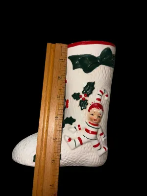 Sale Photo Thumbnail #136: Charming vintage UCAGCO (United China & Glass Company) ceramic Christmas boot planter featuring a whimsical pixie elf dressed in a candy cane-striped outfit, accented with raised holly leaves, berries, and a large green bow. This classic mid-century holid