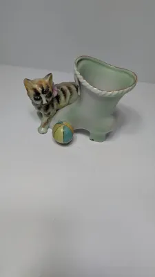Sale Photo Thumbnail #357: The "UCAGCO China Handpainted Japan Cat, Boot, and Ball" is a charming mid-century vintage figurine. Made in Japan by the United China and Glass Company, it usually depicts a small, hand-painted ceramic kitten (often a tabby) either sitting on a boot/shoe