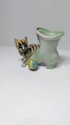 Sale Photo Thumbnail #353: The "UCAGCO China Handpainted Japan Cat, Boot, and Ball" is a charming mid-century vintage figurine. Made in Japan by the United China and Glass Company, it usually depicts a small, hand-painted ceramic kitten (often a tabby) either sitting on a boot/shoe
