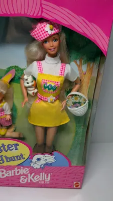 Sale Photo Thumbnail #367: Barbie Doll: Wears a vibrant yellow jumper with an Easter egg pattern pocket, a white t-shirt, a matching pink plaid hat, and shoes.Kelly Doll: Dressed in matching pink plaid overalls, a white t-shirt, and adorable bunny ears.Accessories Included: The set