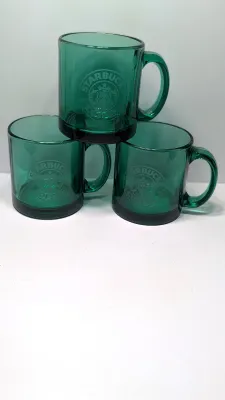Sale Photo Thumbnail #284: This authentic vintage 1990s Starbucks mug is made in the USA from emerald-tinted, clear glass featuring an etched or embossed classic Siren logo