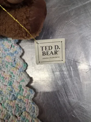 Sale Photo Thumbnail #481: PORCELAIN BABY DOLL IN PINK DRESS, RUSS BERRIE LANGLEY TEDDY BEAR, DEPARTMENT 50 TED D. BEAR PLUSH, ADDITIONAL TEDDY BEAR, AND CROCHETED BABY BLANKET. ALL ITEMS ARE IN PRE-OWNED CONDITION WITH NO VISIBLE MAJOR DAMAGE.