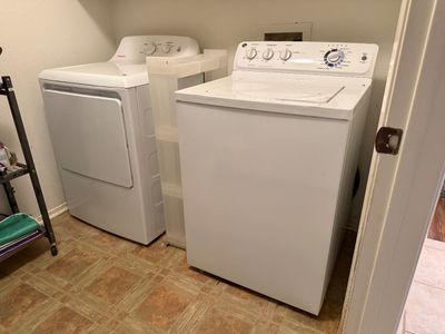 White GE top-load washing machine and Hotpoint front-load dryer set, shown with a slim plastic rolling storage cart between them.