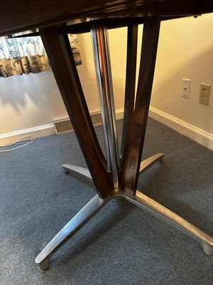 Sale Photo Thumbnail #36: Features a rich walnut-grain laminate veneer surface. It is built with an integrated expansion leaf seam designed to split open for extra seating.Pedestal Base: Supported by a distinctive four-prong cast aluminum and polished chrome "starburst" pedestal b