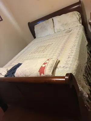 Traditional dark wood sleigh bed frame fitted with a pastel patchwork floral quilt, matching pillow shams, and a folded red-and-white...