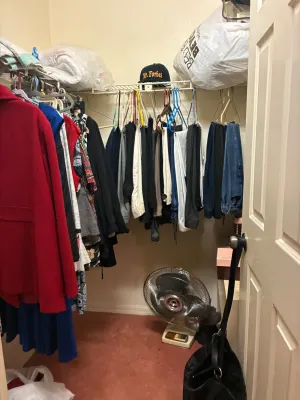 Walk-in closet filled with assorted women's and men's clothing, including coats, pants, and shirts, alongside a vintage white...