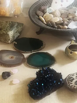 Collection of decorative stones and crystals, including polished agate slices, a dark iridescent cluster, and river rocks.