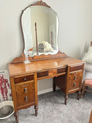 Antique wooden vanity desk with an attached arched mirror, featuring decorative wood inlays, turned legs, and ornate metal drawer pulls.