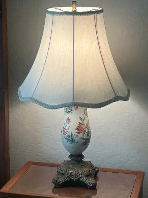 Vintage table lamp featuring a hand-painted floral glass body on an ornate cast metal base, paired with a scalloped fabric shade.