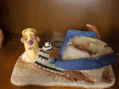 Vintage novelty ceramic ashtray depicting a reclining hillbilly character, showing some wear and discoloration in the bowl.