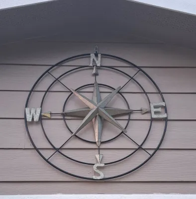 Large metal compass rose wall decor featuring a black iron frame with galvanized metal letters and central star.