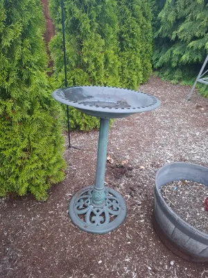 Verdigris-finish metal birdbath featuring an ornate openwork base and a shallow basin with a decorative rim.