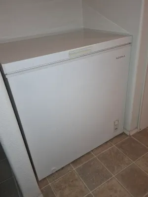 Insignia white chest freezer, showing some light exterior wear, tucked into a tiled alcove.