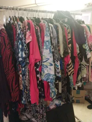 A rolling garment rack filled with a variety of colorful women's clothing, including patterned tops, dresses, and blouses.