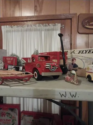 Vintage-style holiday decor including a red metal toy truck with a wreath, a miniature wooden sled, and a Radio Flyer wagon in its...
