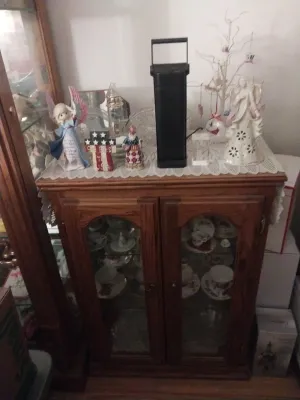 Oak curio cabinet with glass-front doors, displaying various porcelain figurines, teacups, and decorative items on top and inside.