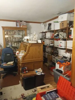 Oak rolltop desk, glass-front display cabinet filled with figurines, and various storage shelves and boxes in a home office setting.