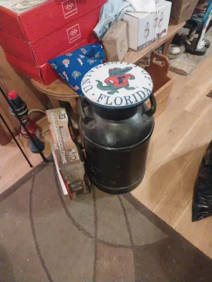 Vintage black metal milk can repurposed as a stool with a padded University of Florida Gators seat cushion.