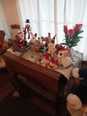 Vintage wooden drop-leaf tea cart displaying an assortment of Christmas decorations, including Santa figurines, a plush reindeer, and a...