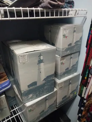 Collection of boxed Harbour Lights lighthouse figurines, including the Gay Head Massachusetts model, stacked on closet shelving.