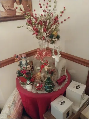 Assorted Christmas decorations, including a white reindeer figurine, a patriotic Santa Claus, and a festive floral arrangement in a glass...