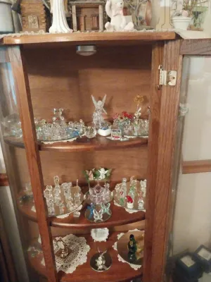 Vintage oak curio cabinet with curved glass sides, featuring three shelves filled with various glass and crystal figurines.
