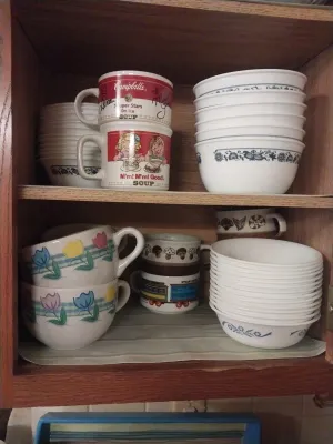 Assortment of vintage kitchenware, including Pyrex Old Town Blue bowls, Campbell's Soup mugs, and retro tulip-patterned soup mugs.