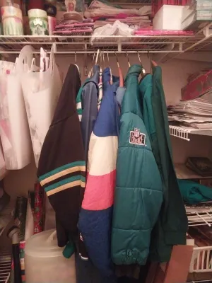 Assorted vintage jackets hanging in a closet, including a green NFL Experience puffer jacket and a color-blocked windbreaker.