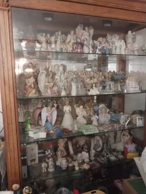 Large collection of angel and holiday-themed figurines displayed inside a lighted wooden curio cabinet with glass shelves.