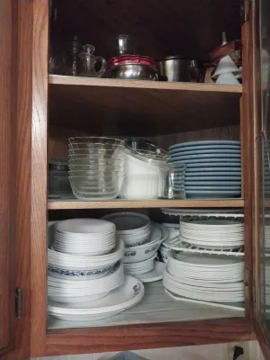 Assorted kitchenware and dinnerware, including Corelle plates and bowls, clear glass nesting bowls, and various serving pieces, stored in...