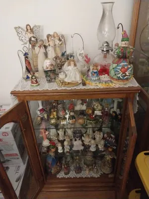 Wooden curio cabinet with glass shelves filled with various angel figurines, a glass hurricane lamp, and other decorative collectibles.