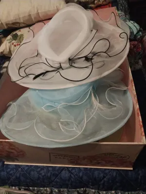 Two vintage-style wide-brimmed organza dress hats, one in white with black piping and feathers, and one in light blue with white piping,...