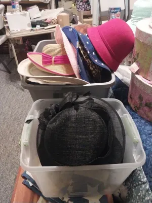 Assortment of women's hats, including a black woven straw hat with a bow, a pink felt cloche, and various straw sun hats, stored in...